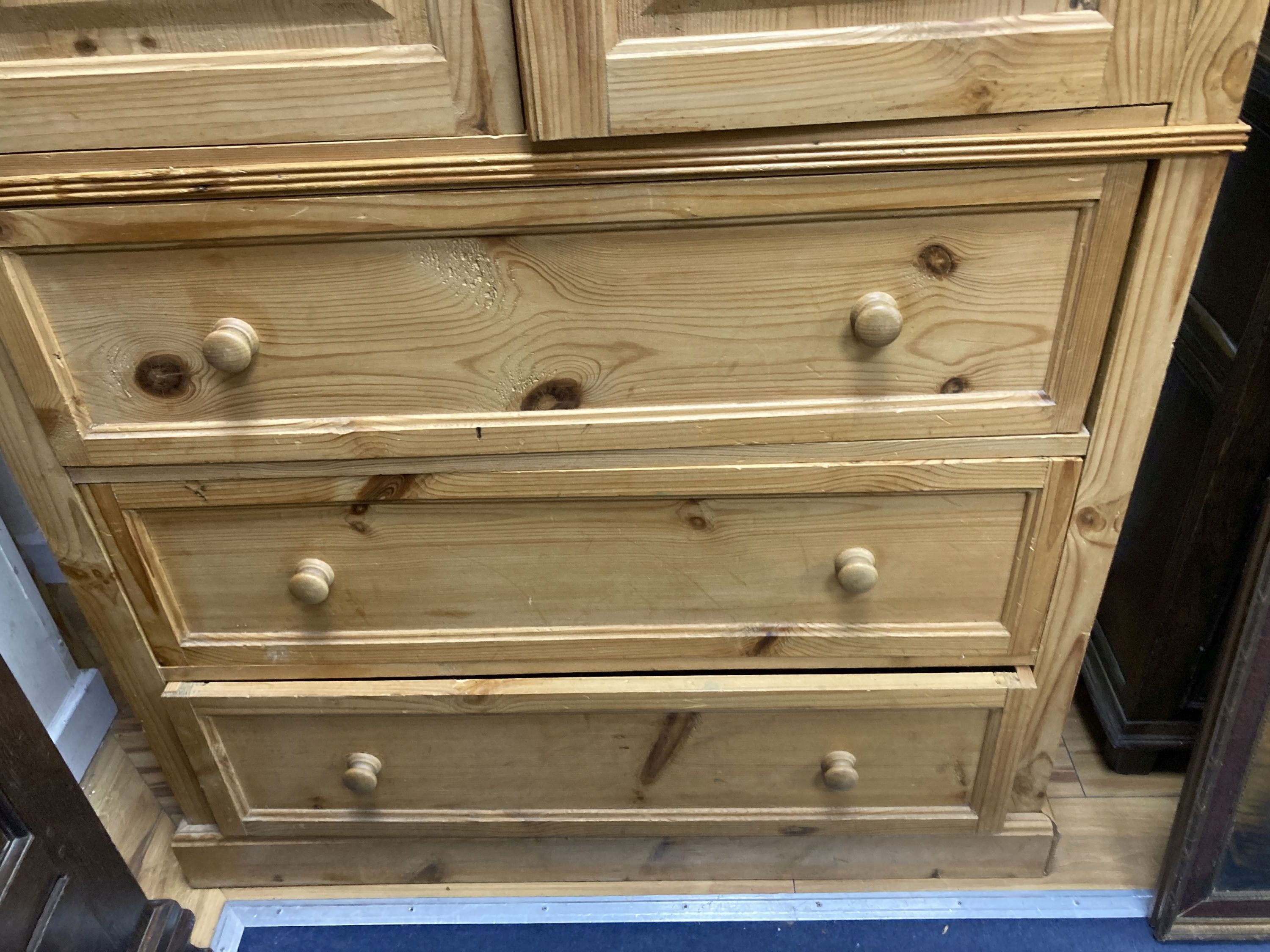 A contemporary pale pine press cupboard with twin panelled cupboard doors over a base fitted with three long drawers, height 199cm, width 105cm depth 57cm